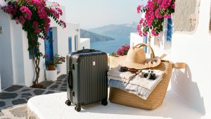 Valise cabine entourée d’accessoires de voyage devant un décor méditerranéen inspiré des îles grecques.